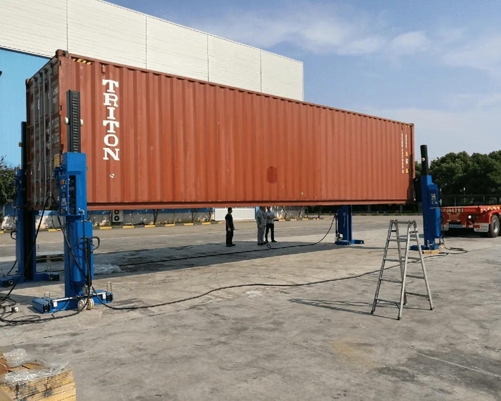 Four hydraulic container lift jacks raising a loaded shipping container, each with its own control panel