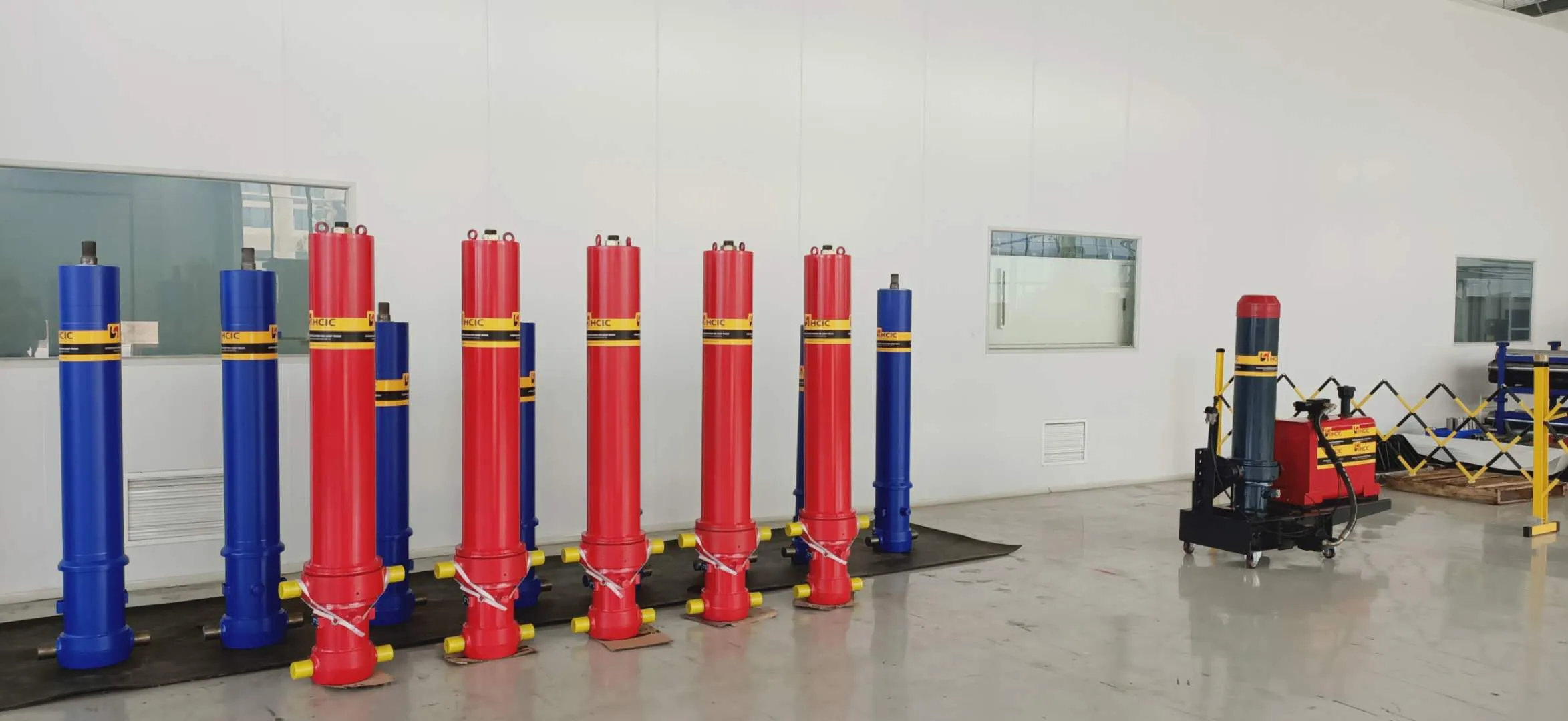 Row of red and blue telescopic front-end cylinders on the factory floor before assembly